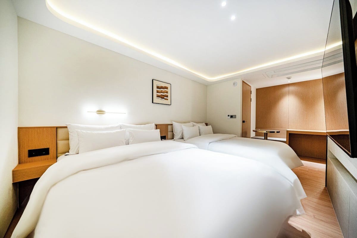 Una habitación de hotel con una cama grande, mesitas de noche, una lámpara de pared y un armario de madera.