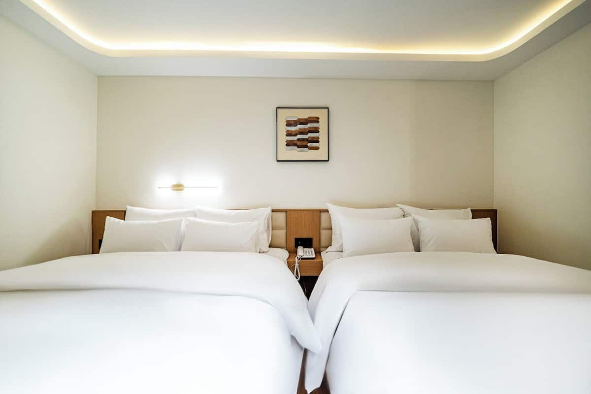 Habitación de hotel con dos camas, una mesita de noche con teléfono, y una lámpara de pared.
