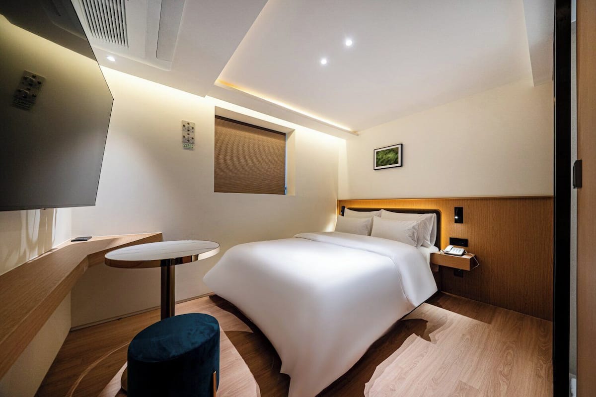 Una habitación de hotel moderna con una cama, una mesita de noche y una pequeña mesa redonda.