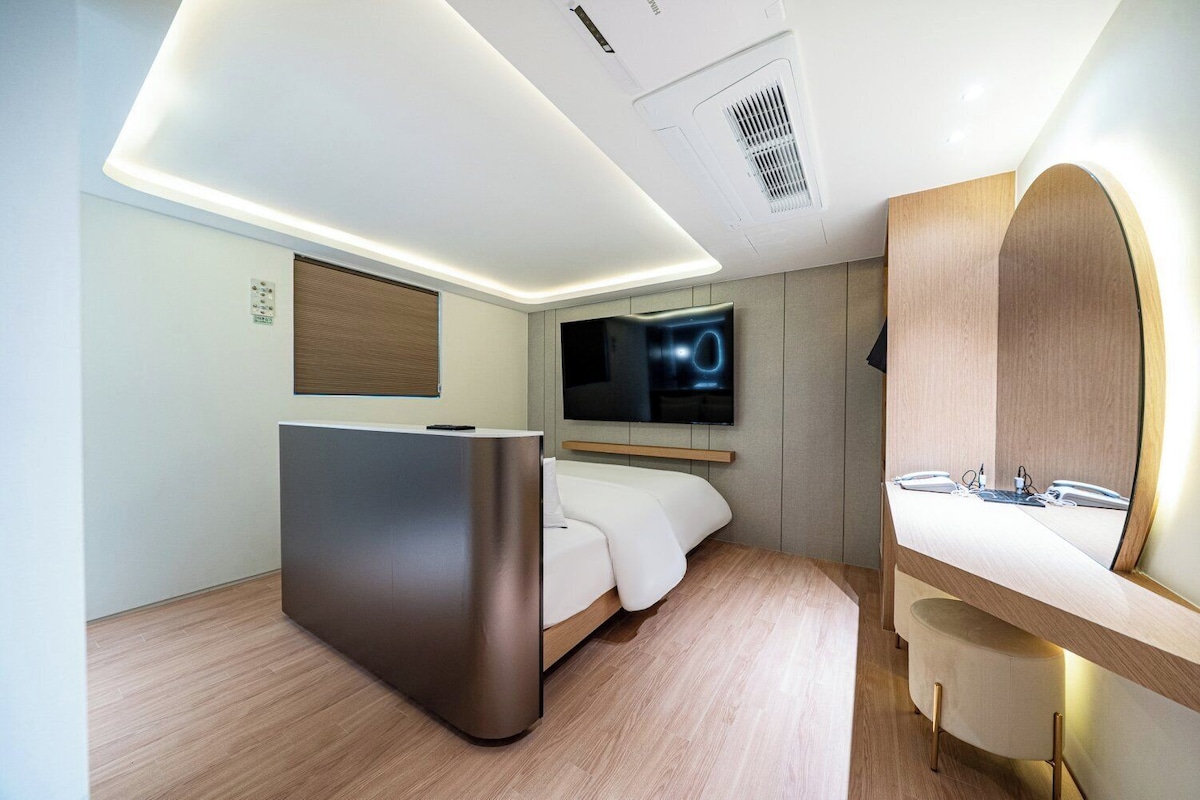 A modern hotel room with a bed, a desk, a TV, and a mirror.
