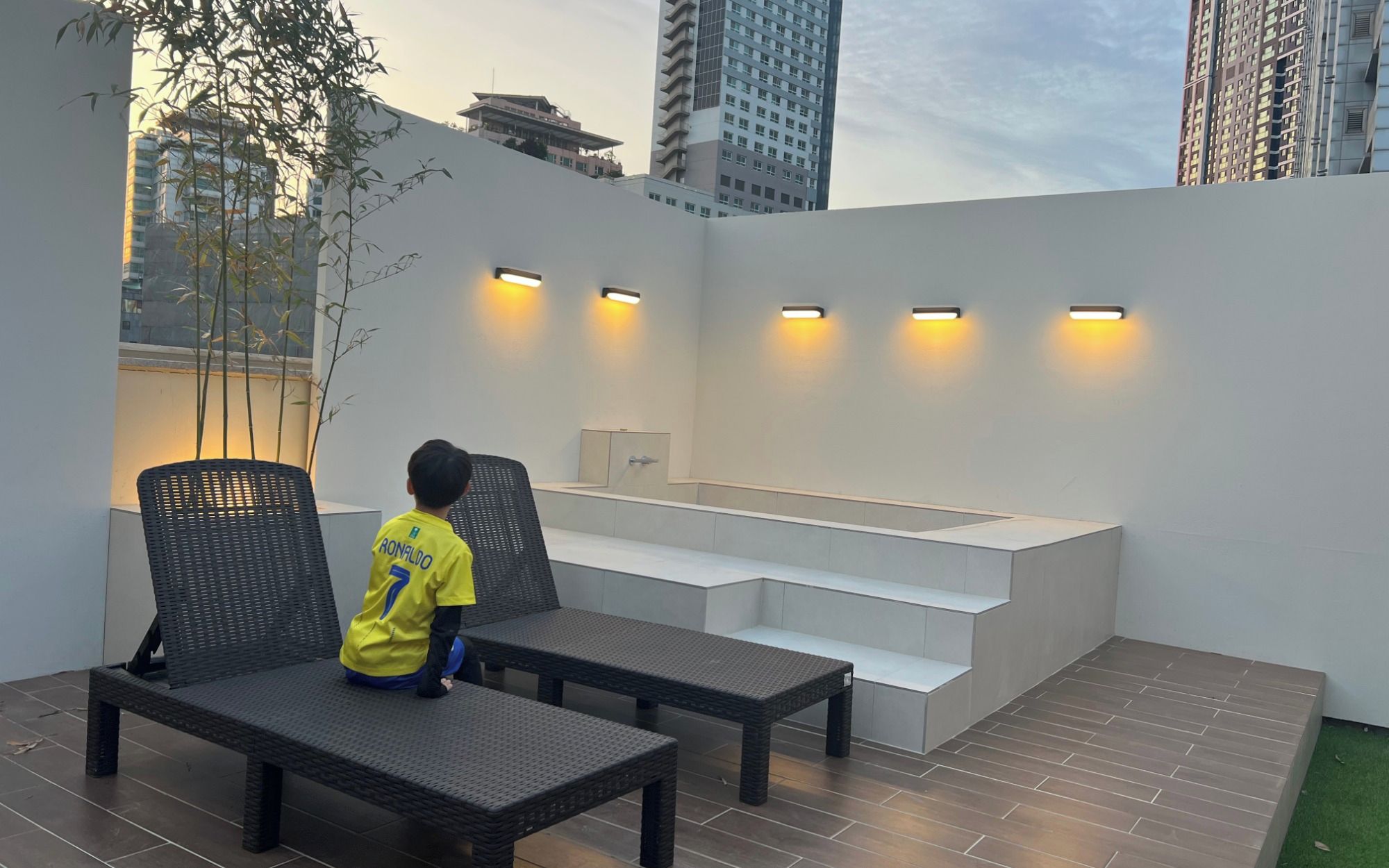 Niño sentado en un banco en un espacio al aire libre con diseño moderno, que incluye un mostrador blanco y escalones.