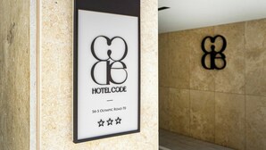 A falra szerelt táblán a logó és a „HOTEL CODE” felirat, valamint a cím található.