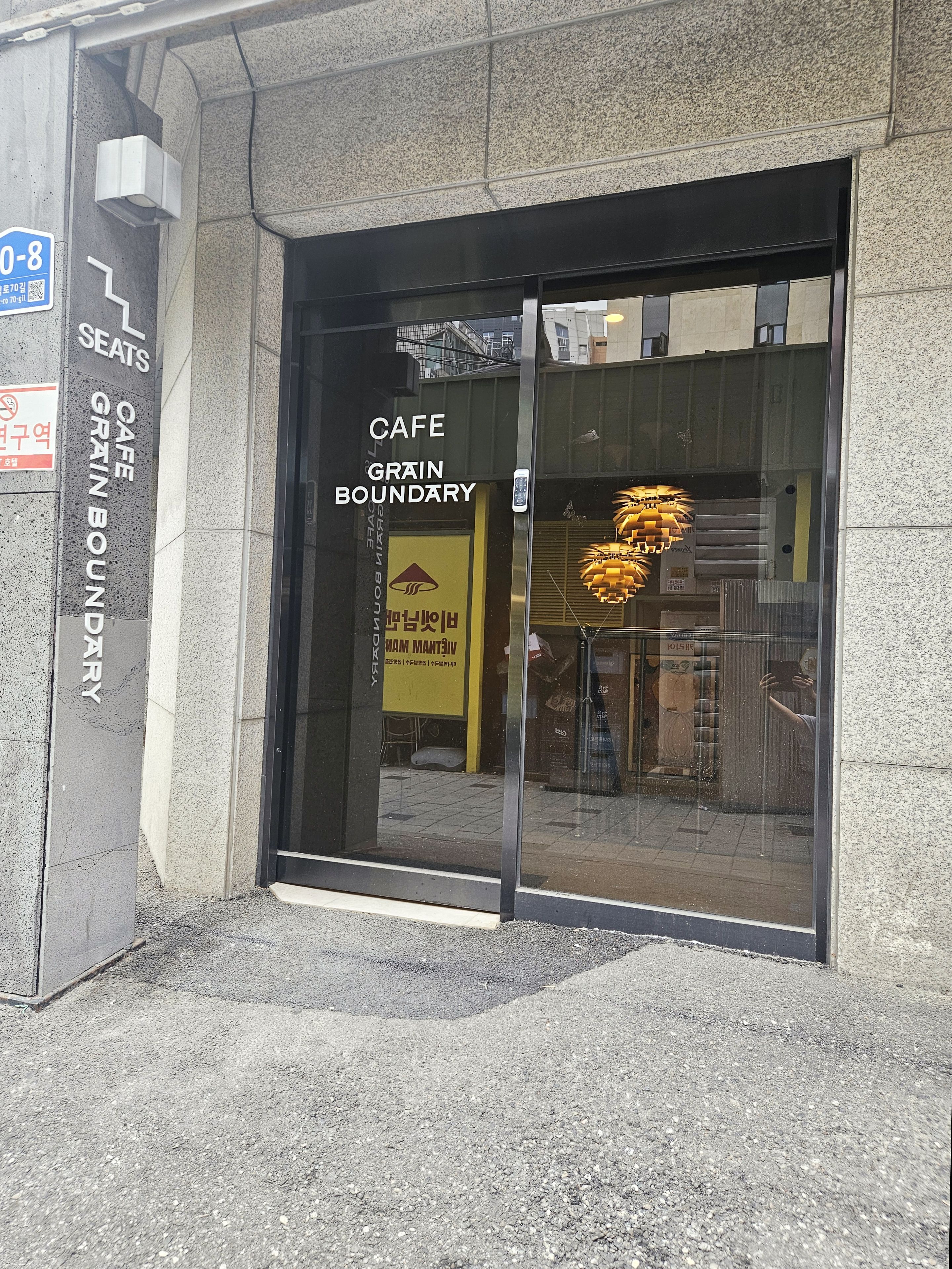 L'ingresso di un edificio con una porta in vetro, un cartello che indica 'CAFE GRAIN BOUNDARY' e un'insegna con la scritta 'SEATS' che segnala la disponibilità di posti a sedere.