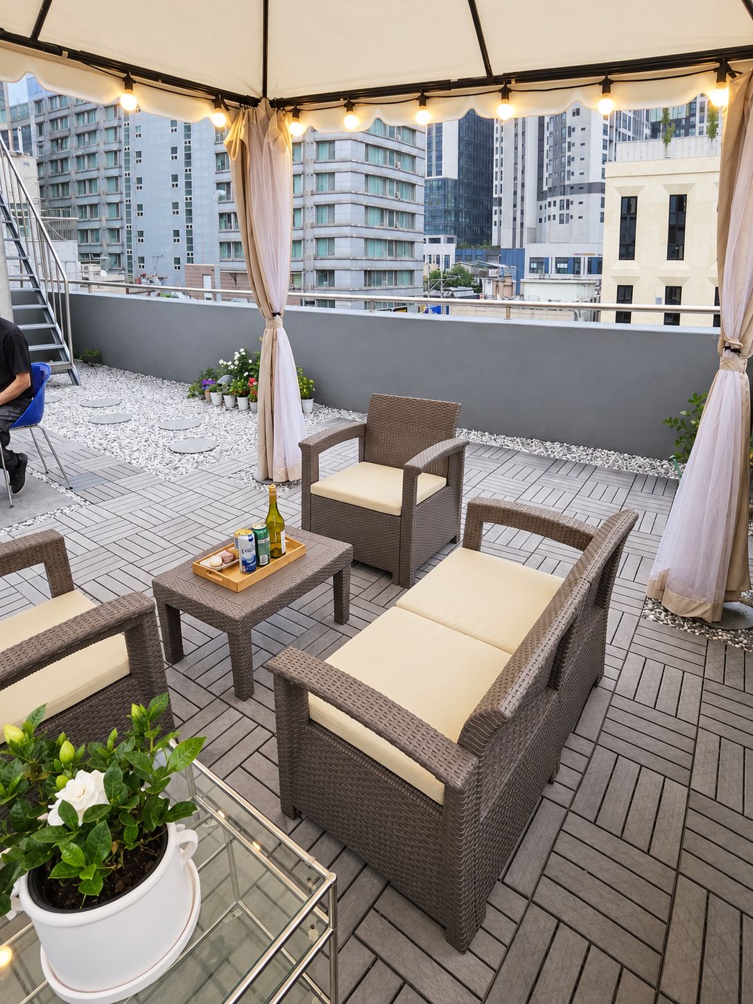 Terraço no telhado com mobiliário de vime, mesa de vidro e um vaso de planta.