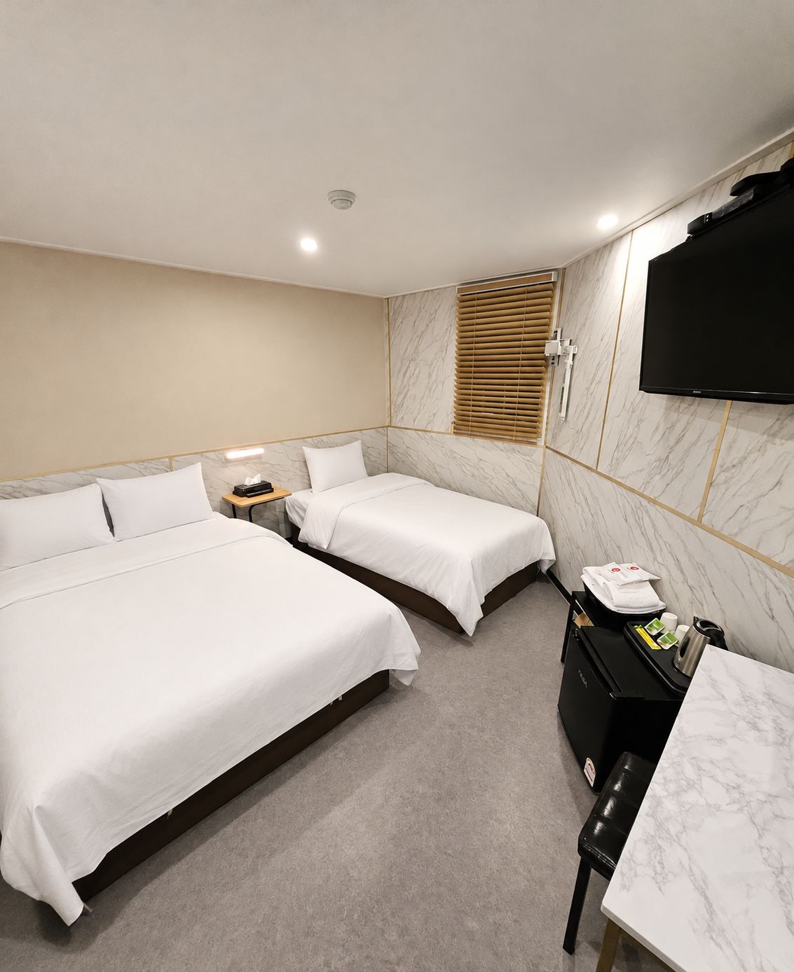 A hotel room with two beds, a desk, a TV, and a minibar.