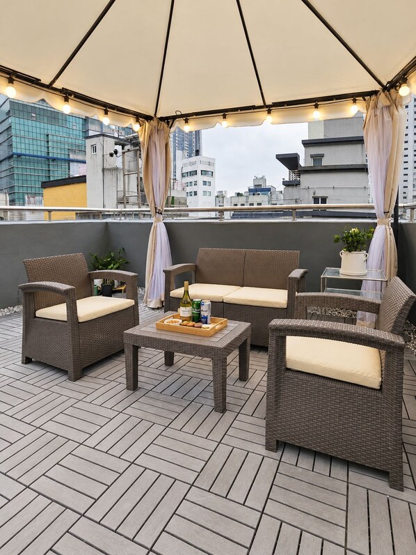An outdoor patio with wicker furniture, a table with a tray of snacks and drinks, and a view of city buildings.