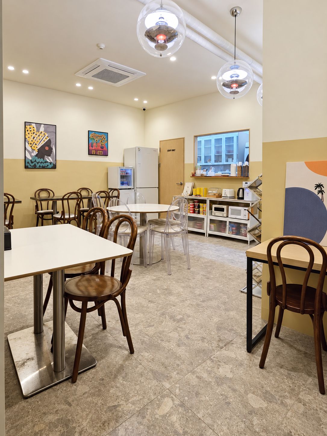 A modern kitchen with a dining area, equipped with stainless steel appliances, clear chairs, and a tiled floor.