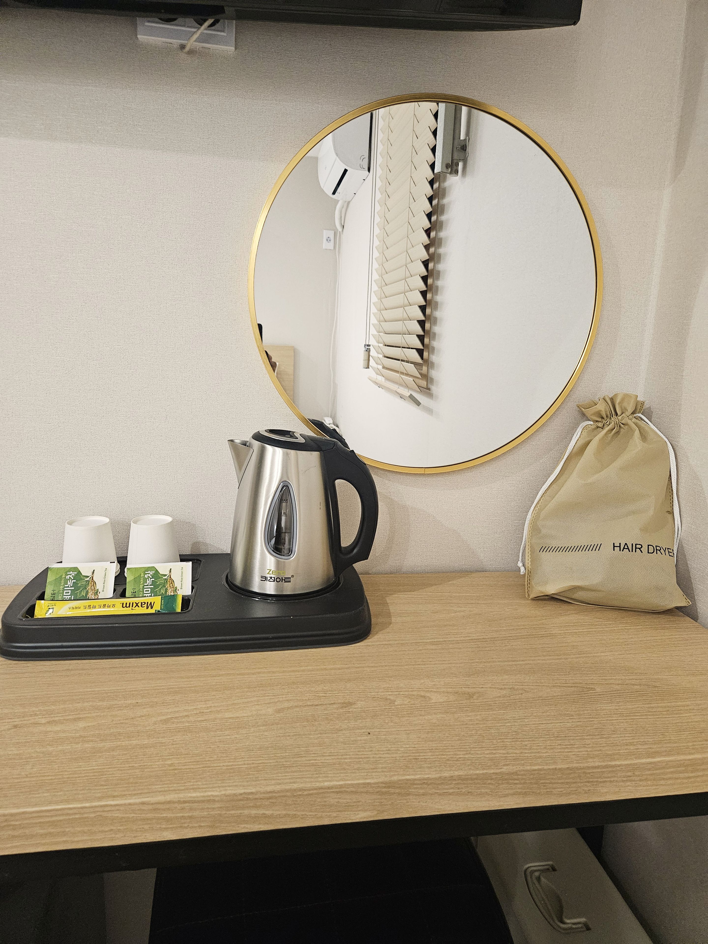 A hotel room with a coffee maker, a hair dryer, and a small bag on the table.