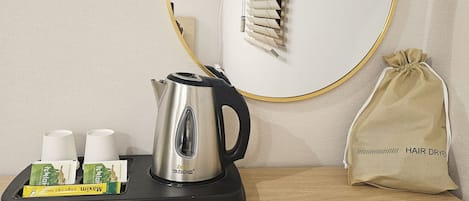 Quarto de hotel com cafeteira, secador de cabelo e uma pequena bolsa sobre a mesa.