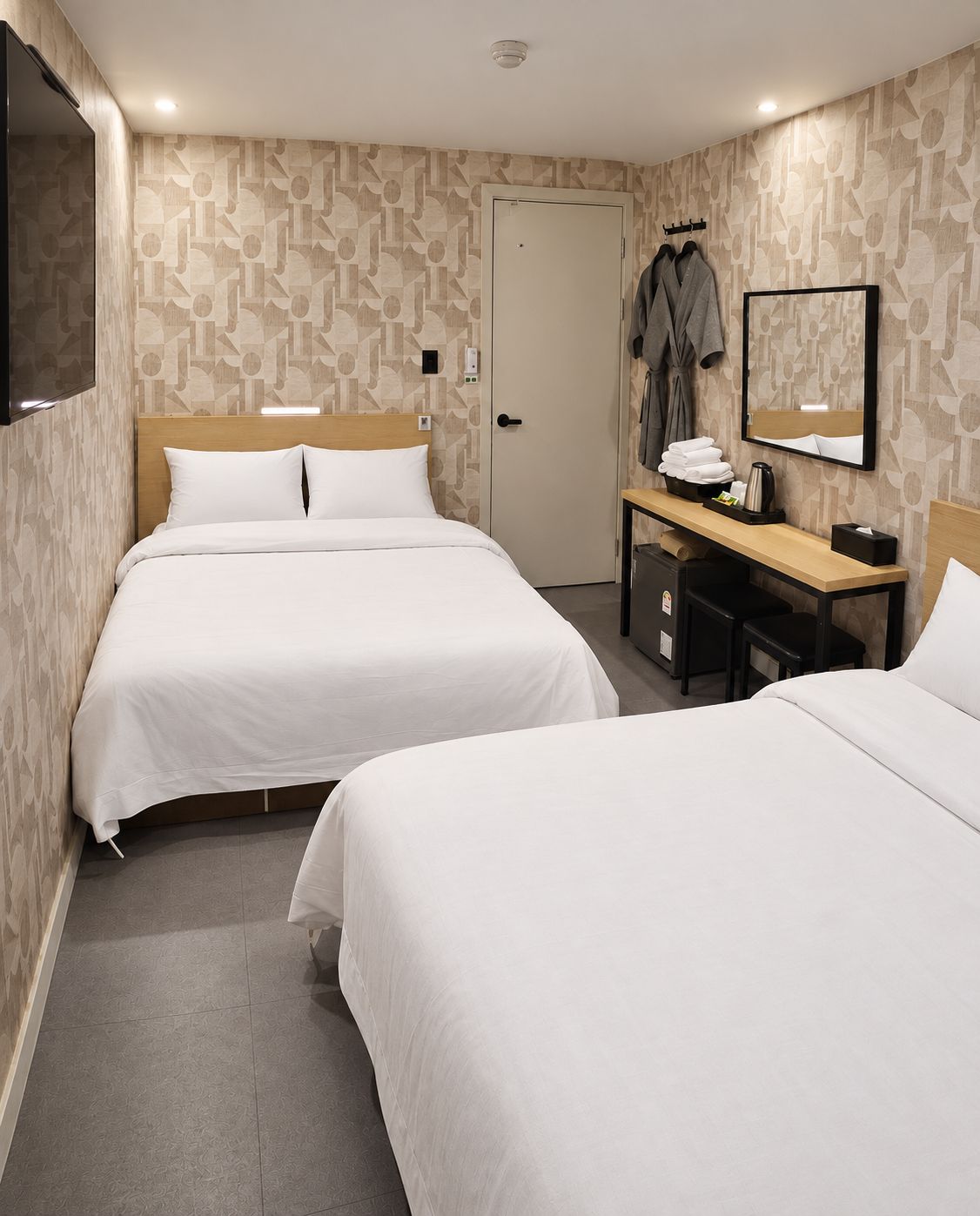 A hotel room with two beds, a desk with a chair, a coat rack, and a mirror.