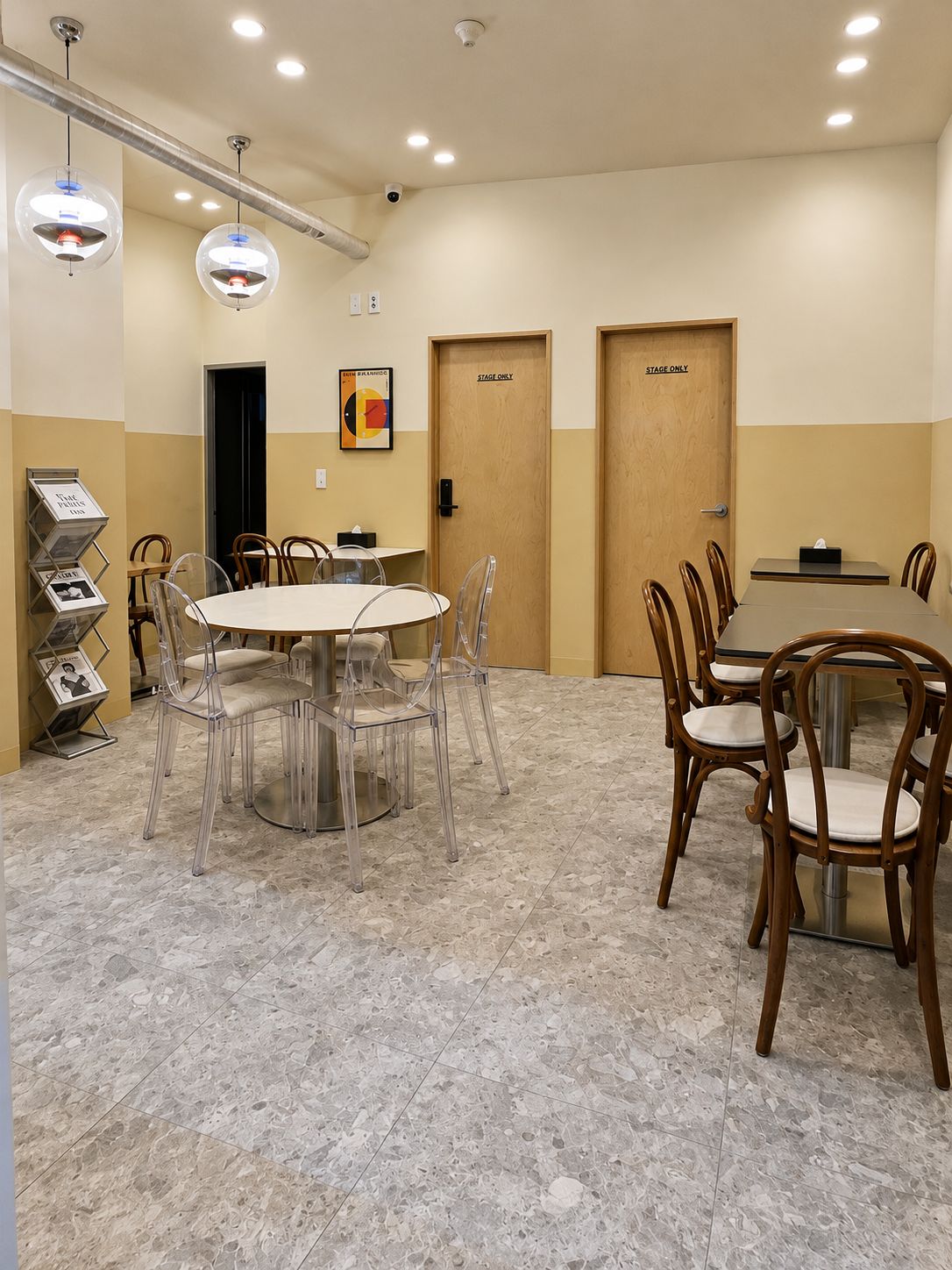 Sala de conferência com mesa redonda, cadeiras e tela de projetor. Há duas portas identificadas como 'Apenas Palco' e um cartaz na parede.