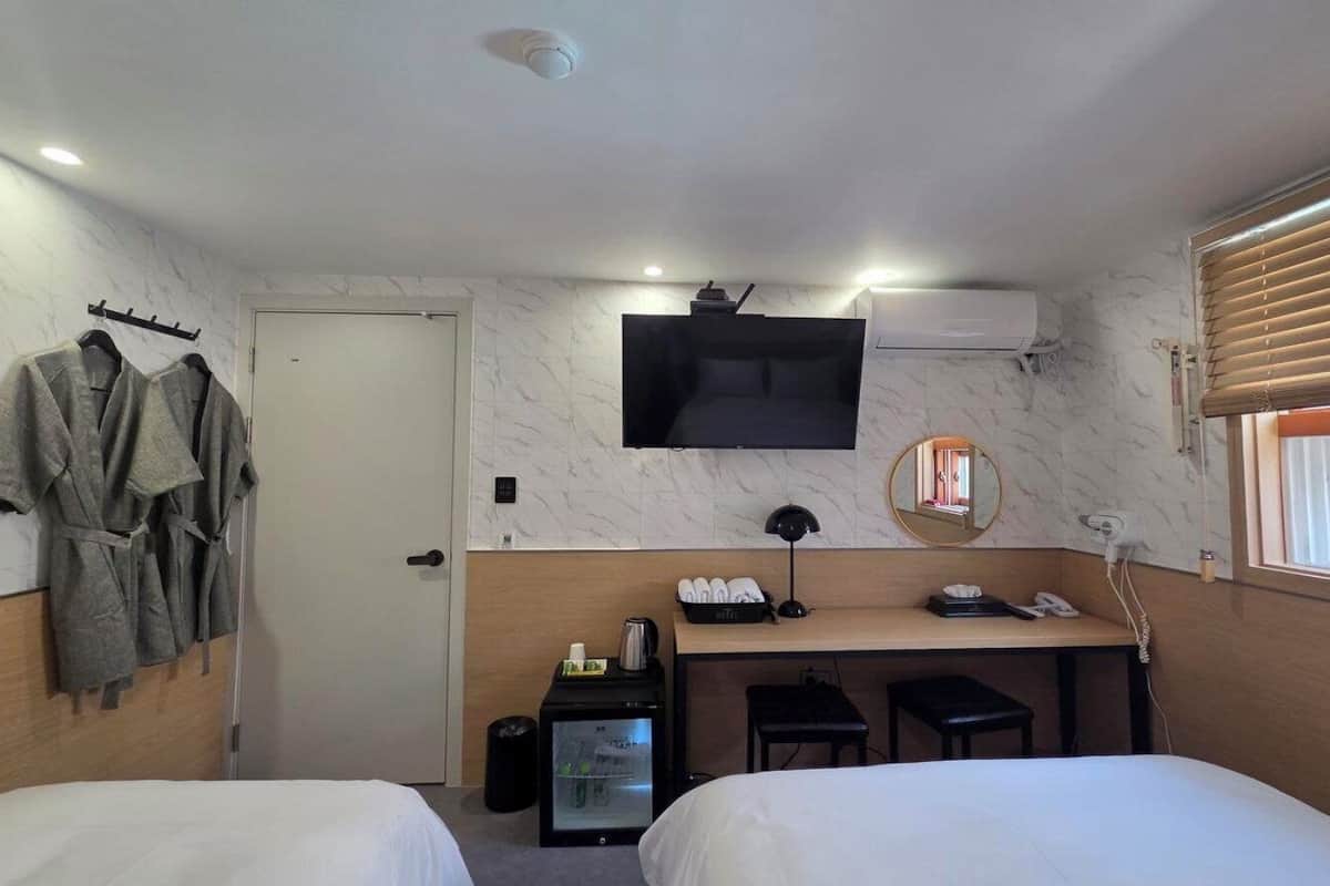 Une chambre d’hôtel avec deux lits, un bureau doté d’un téléviseur à écran plat, un miroir, une machine à café et une fenêtre avec des stores.