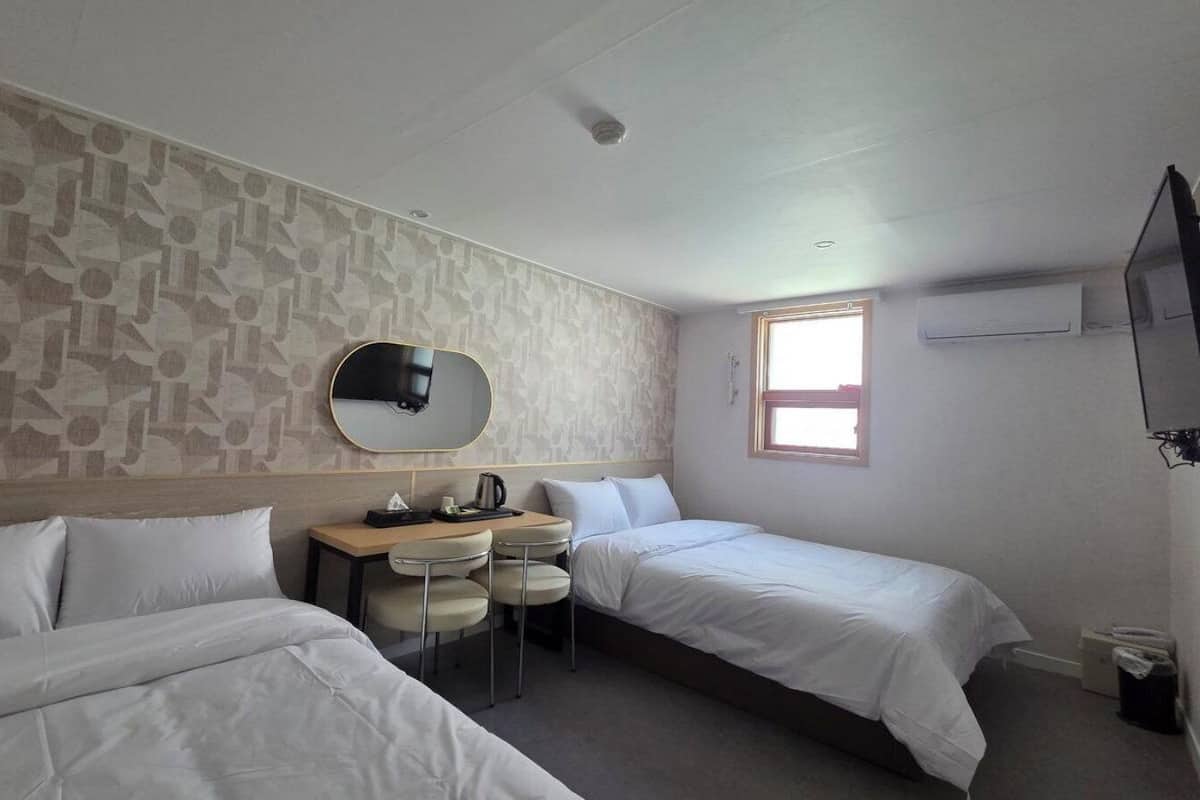 Une chambre d’hôtel avec deux lits, un bureau avec des chaises, une télévision et une fenêtre.