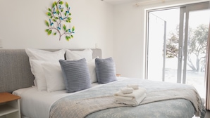 A bedroom with a bed, pillows, a blanket, a wall art piece, and a view through a glass door. - 2 Bedroom Beach Frontage Apartment (Paihia)