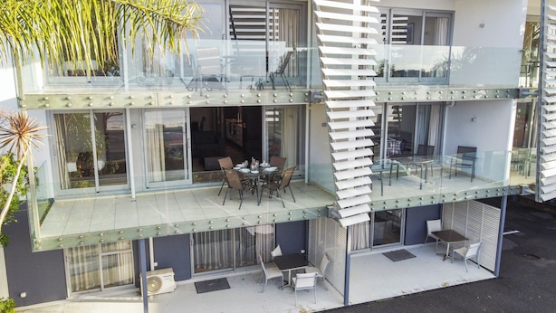 A modern two-story building with a glass balcony, outdoor seating, and a view of the surrounding area. - 2 Bedroom Beach Frontage Apartment (Paihia)