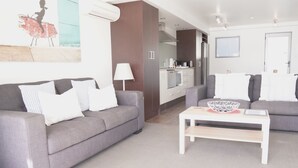 A modern living room with two grey sofas, a white coffee table, and a kitchen area in the background. - 2 Bedroom Beach Frontage Apartment (Paihia)