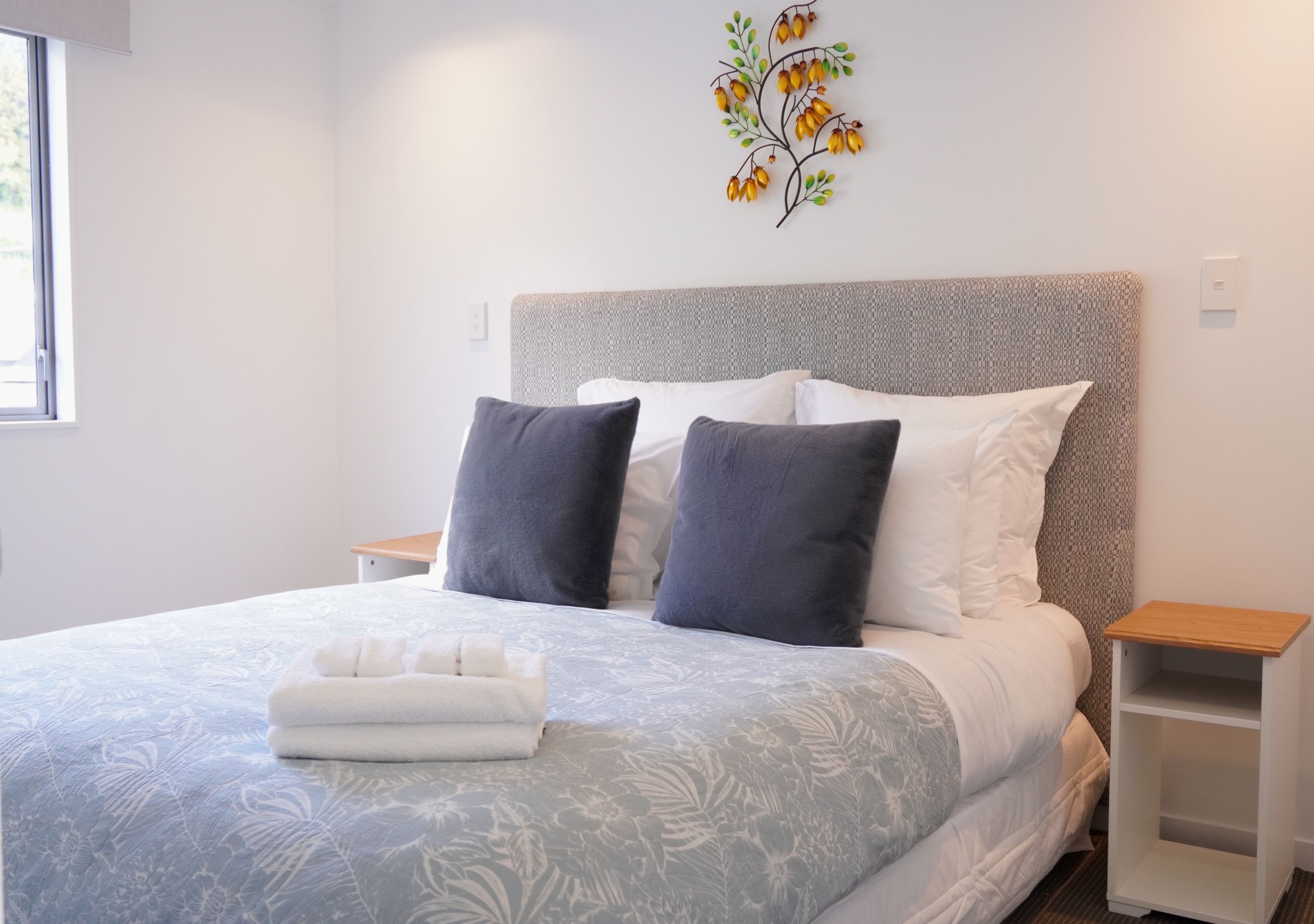 A neatly made bed with a patterned bedspread, two pillows, and a folded towel.