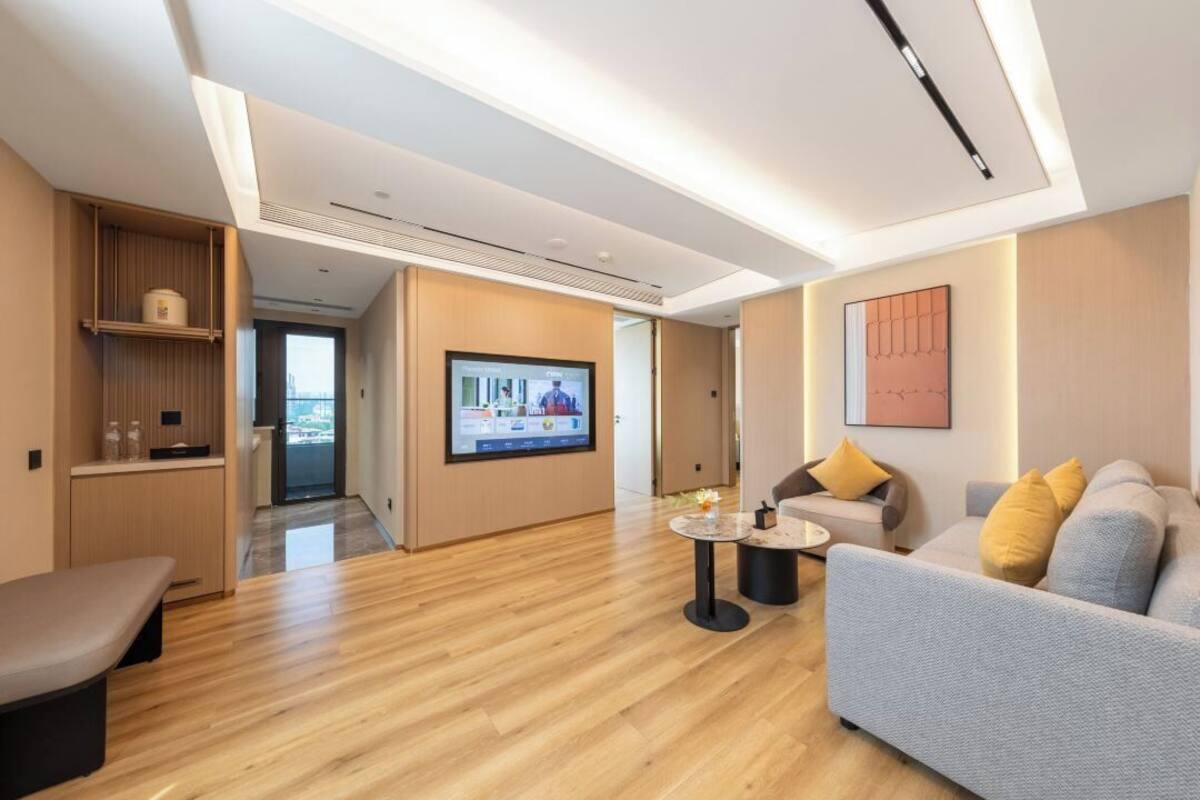 Una habitación de hotel moderna con suelo de madera, un sofá, una mesa de centro, un televisor y una obra de arte colgada en la pared.
