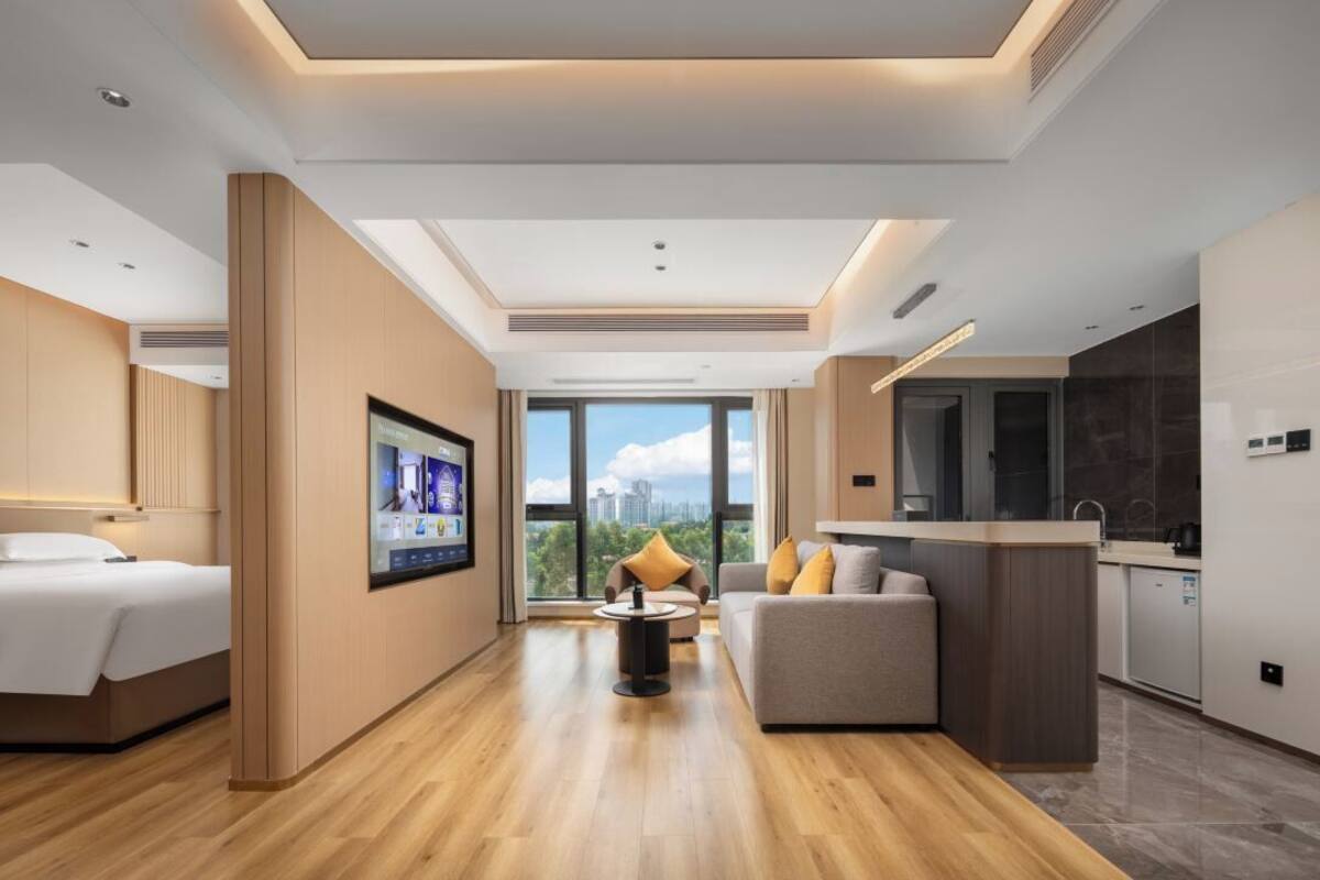 Una habitación de hotel moderna con cama, sofá, una mesita, televisión y zona de cocina.