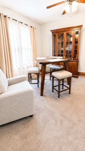 Ein Wohnzimmer mit einer Couch, einem Esstisch mit zwei Stühlen, einem Holzschrank und einem Deckenventilator.