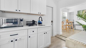 Een moderne keuken met witte kastjes, een magnetron, een spoelbak en een eethoek met een tafel en stoelen.