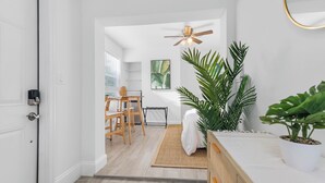 Een moderne, goed verlichte kamer met een plafondventilator, een bed met een witte hoofdbord, een houten bureau en een grote potplant.