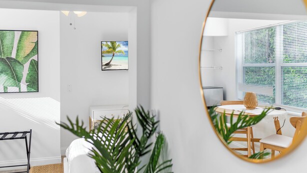 Een moderne kamer met een bed, een eethoek met een tafel en stoelen, een grote spiegel en kunstwerken aan de muur.