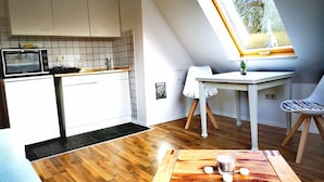 Kompakti keittiö, jossa on valkoiset kaapit, mikroaaltouuni sekä pieni ruokailutila, jossa on pöytä ja tuolit.