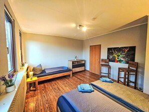 Une pièce comprenant un lit, un petit bureau, une chaise, une fenêtre et un tableau accroché au mur.