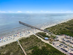 Vista aerea di una spiaggia con un molo, un parcheggio e un edificio con tetto blu.