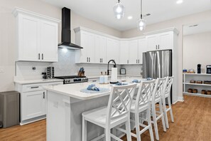 A modern kitchen with white cabinetry, a stainless steel refrigerator, and a central island with bar stools. - New Construction 4BR Golf Retreat - Golf Course Views - 3 Miles to Sunset Beach (Sunset Beach)