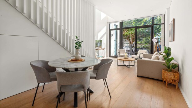Ein modernes Interieur mit Essbereich, Treppe und einer Sitzgelegenheit mit Blick auf Grünflächen.