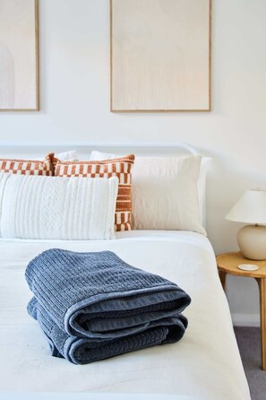 A neatly made bed with a folded blanket, white pillows, and a bedside table with a lamp.