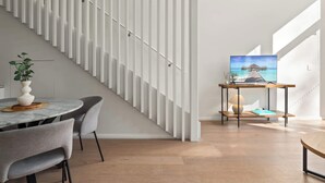 Ein modernes Interieur mit einer Treppe, einem Essbereich mit einem Marmortisch und einem Fernseher, der eine tropische Szene zeigt.