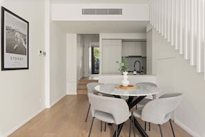 Uma área de refeições moderna com uma mesa redonda, cadeiras estofadas cinzas e um vaso branco com uma planta.