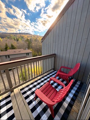 Een balkon met een geruit vloertje, twee rode stoelen en uitzicht op een glooiend landschap.