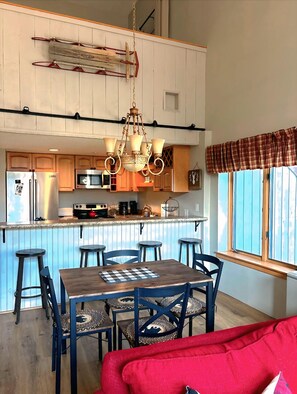 Een keuken met een centraal eiland, houten kasten, een kroonluchter en een zithoek met een rode bank.