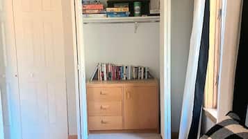 Un dormitorio con cama, armario, estante con libros y juegos, y ventana con cortinas.