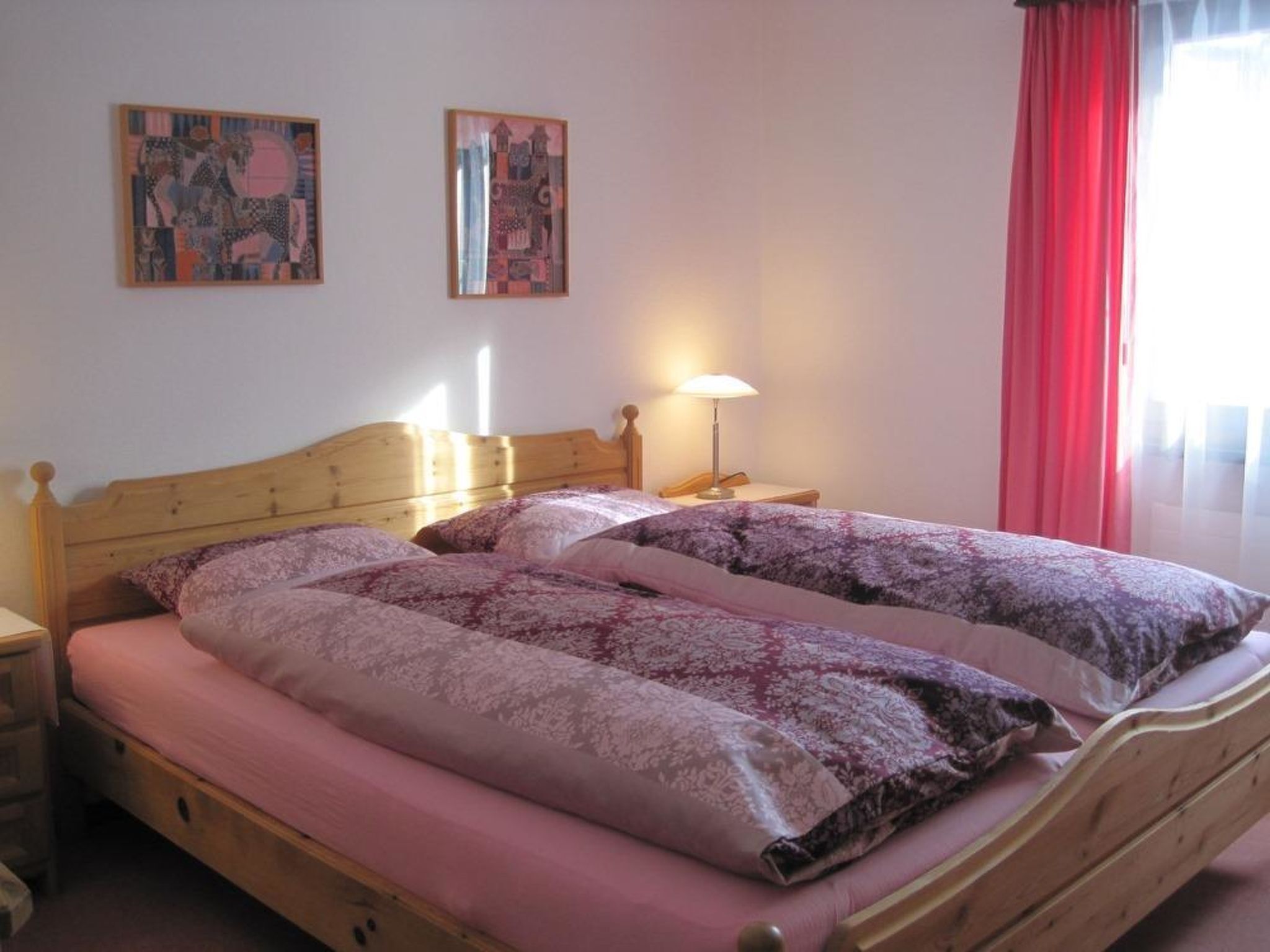 Ein Doppelbett mit Holz-Kopfteil, ein Nachttisch mit Lampe und zwei gerahmte Kunstwerke an der Wand.