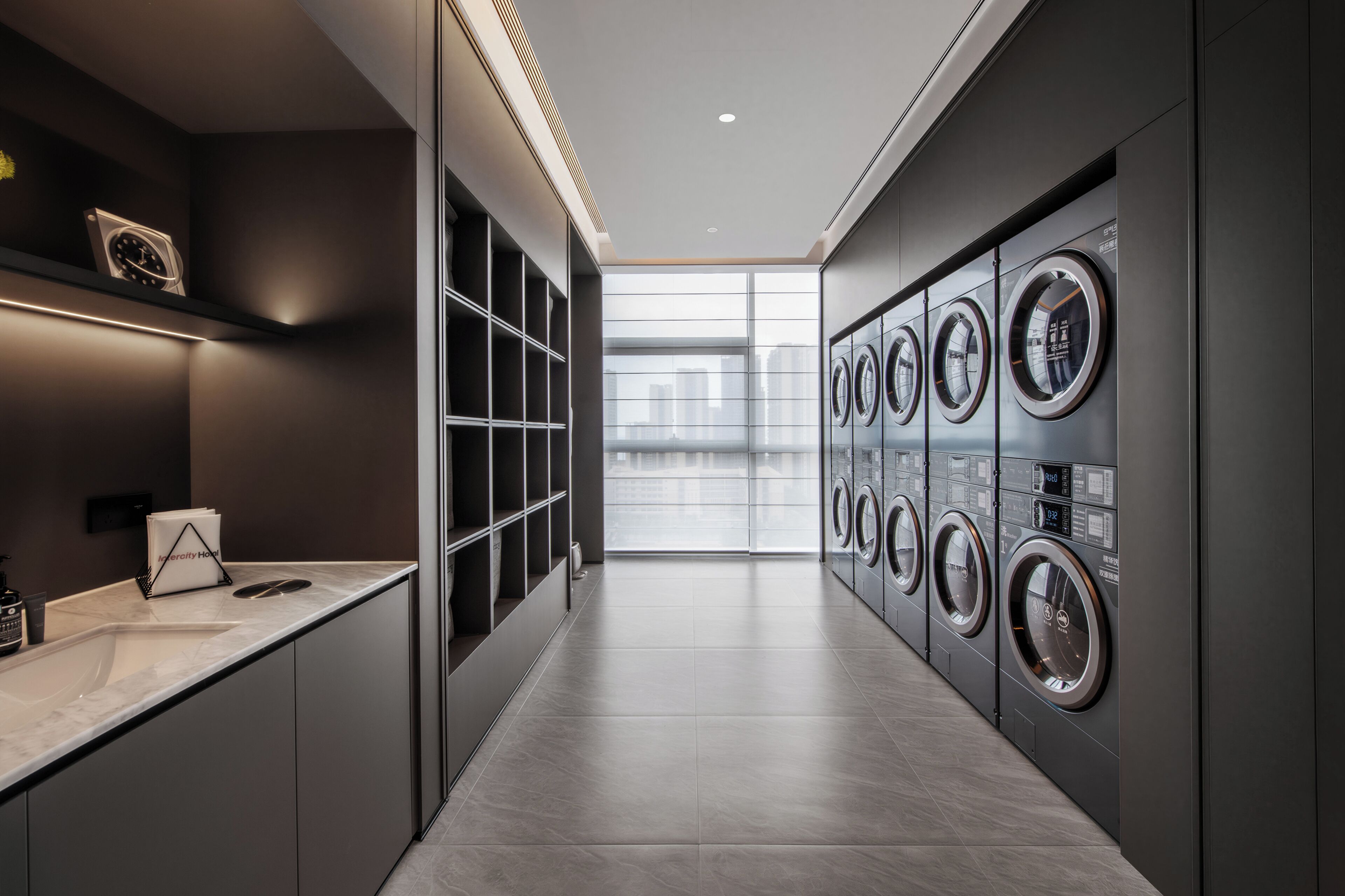A modern laundry facility with multiple washing machines, a marble countertop, and a view of the city through large windows.