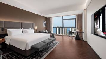 A modern hotel room with a large bed, a desk, a chair, and a view of the city.