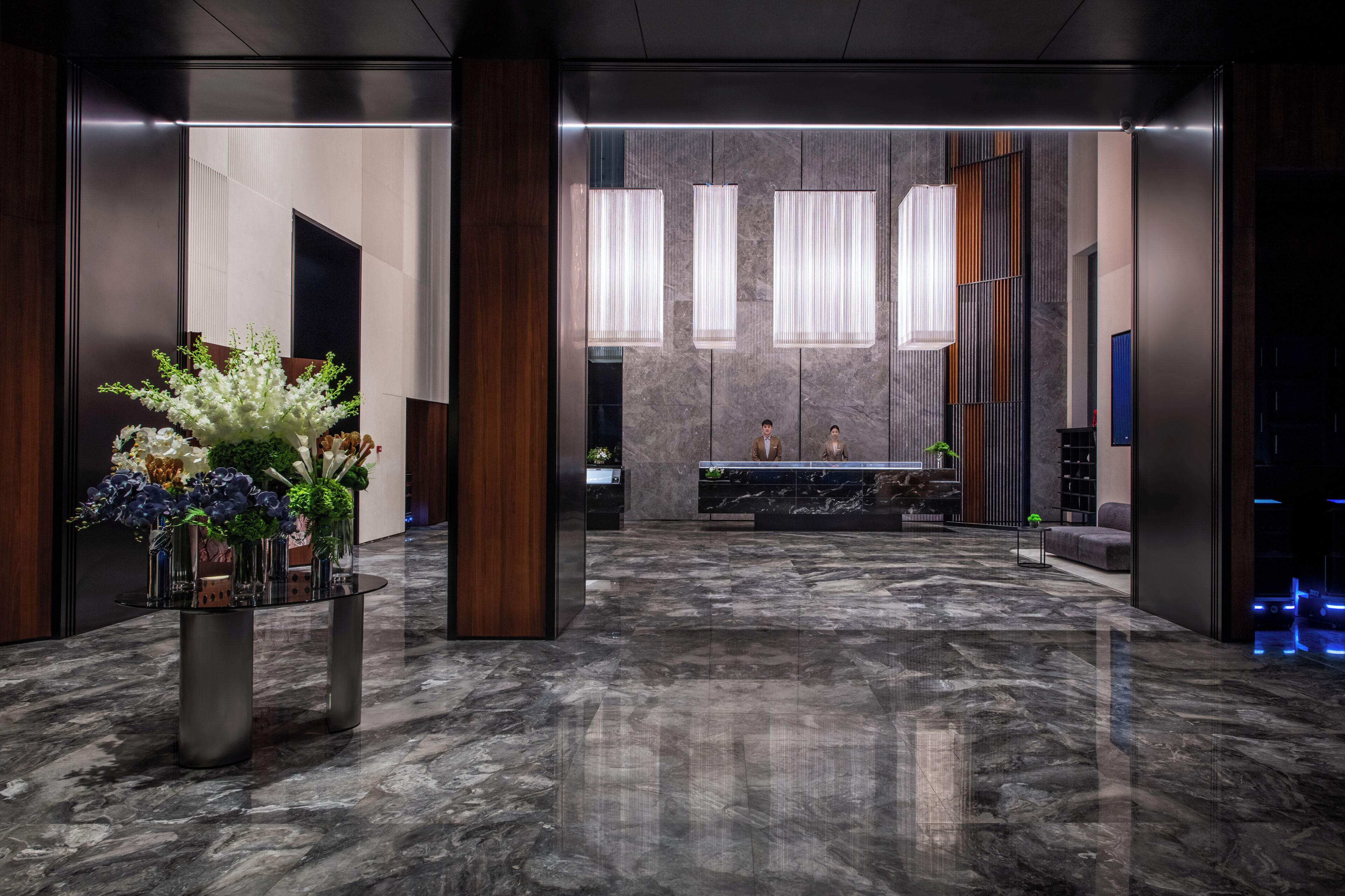 A modern lobby with a reception desk, marble flooring, and decorative plants.