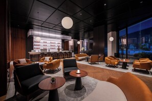 A modern lounge area with seating, a bar, and a large window offering a view of the cityscape.