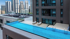 A rooftop swimming pool with lounge chairs and a glass balustrade.