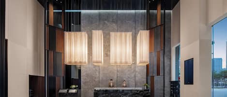 A modern lobby with a reception desk, three pendant lights, a marble floor, and a large window.