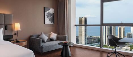 Una habitación de hotel moderna con un ventanal grande, un sofá, una mesita y una cama.