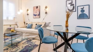 A modern living room with a sofa, a glass coffee table, and blue chairs around a glass dining table. - Atocha VI (Madrid)