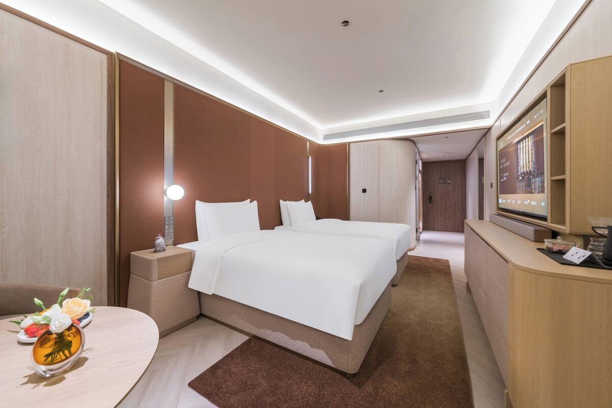 Una habitación de hotel con cama, mesitas de noche, escritorio, espejo y televisor.
