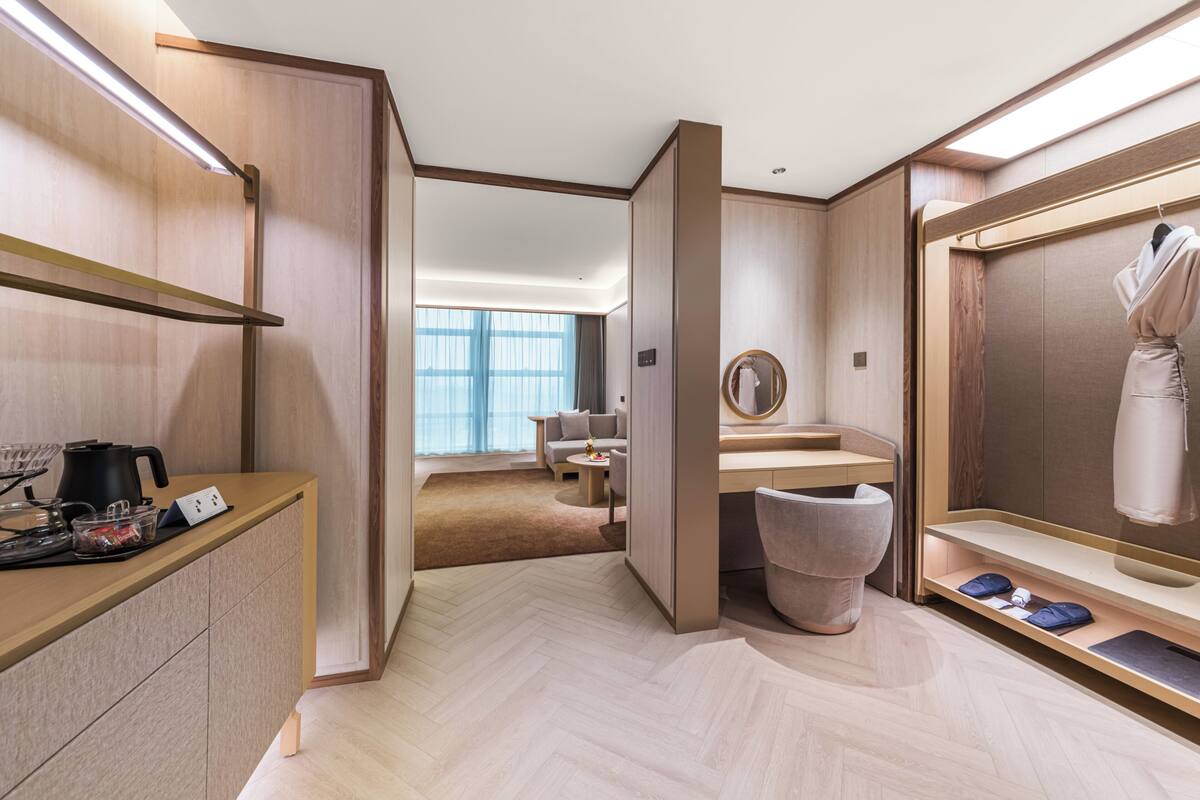 Habitación de hotel moderna con piso de madera, un escritorio con espejo, una bata colgada y vista a un área de estar.