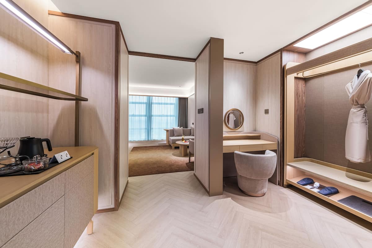 Moderni hotellihuone, jossa on puulattia, peilillä varustettu työpöytä, naulakko ja näkymä oleskelutilaan.
